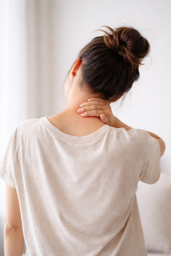 Woman holding neck showing symptoms of breast implant illness such as muscle pain and fatigue.